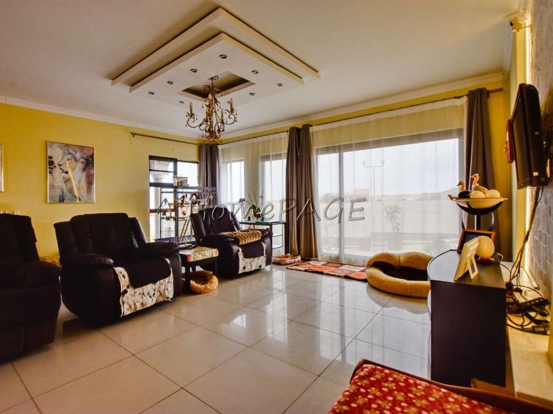 Spacious living room featuring a decorative tray ceiling with recessed lighting, large sliding glass doors, and polished porcelain floor tiles.