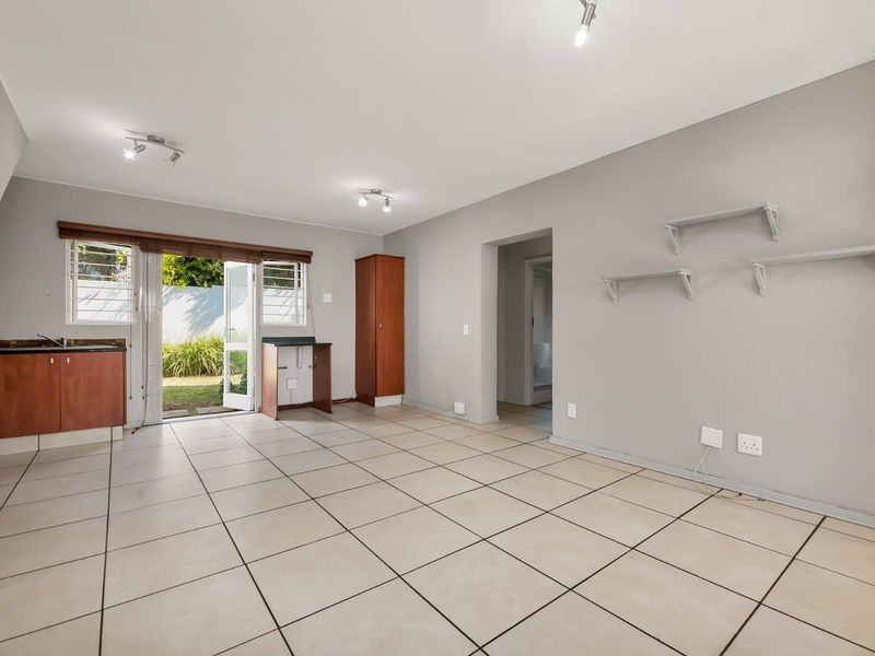 Open-plan living area featuring tiled floors, a compact kitchenette, and direct access to the rear garden through a sliding glass door.