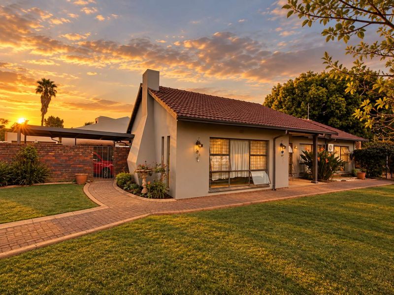 Charming single-story home featuring a tiled roof, brick chimney, and a well-maintained front garden with a paved walkway and carport at sunset.