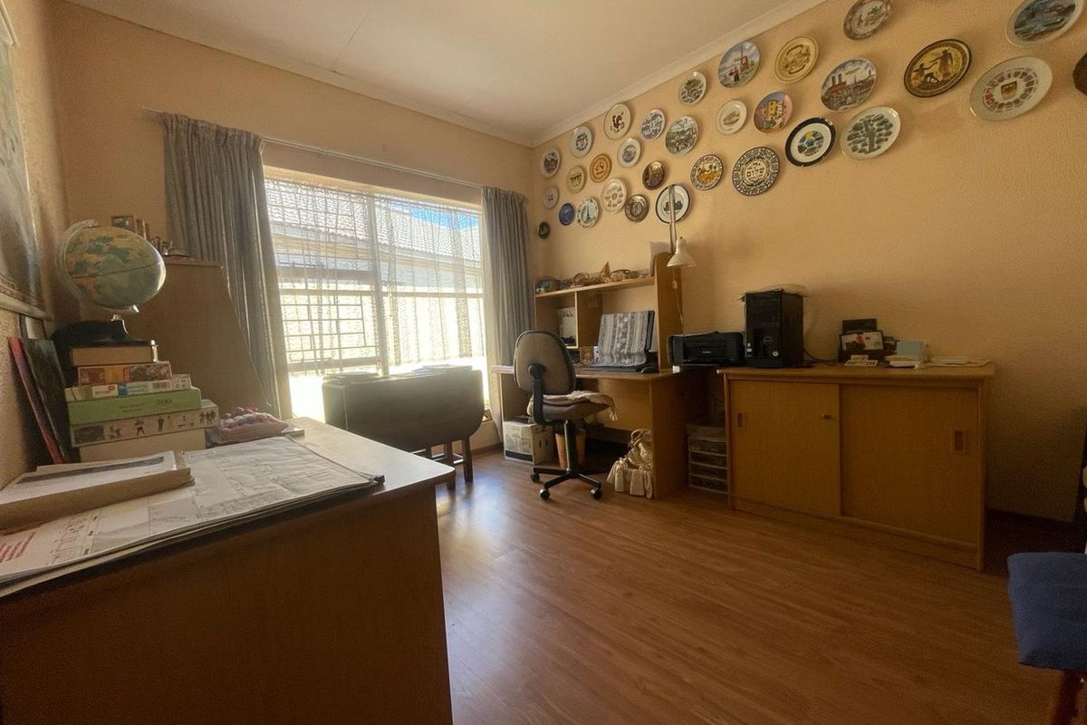 A functional bedroom or home office space featuring laminate flooring, a large window with curtains, and neutral wall finishes.