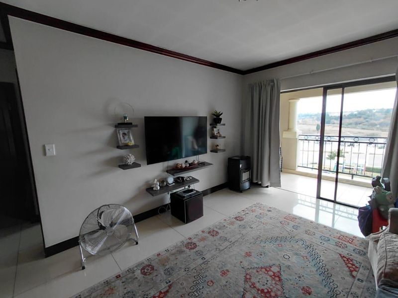 A living room featuring tiled flooring, dark crown molding, and sliding glass doors that open onto a balcony with scenic views.