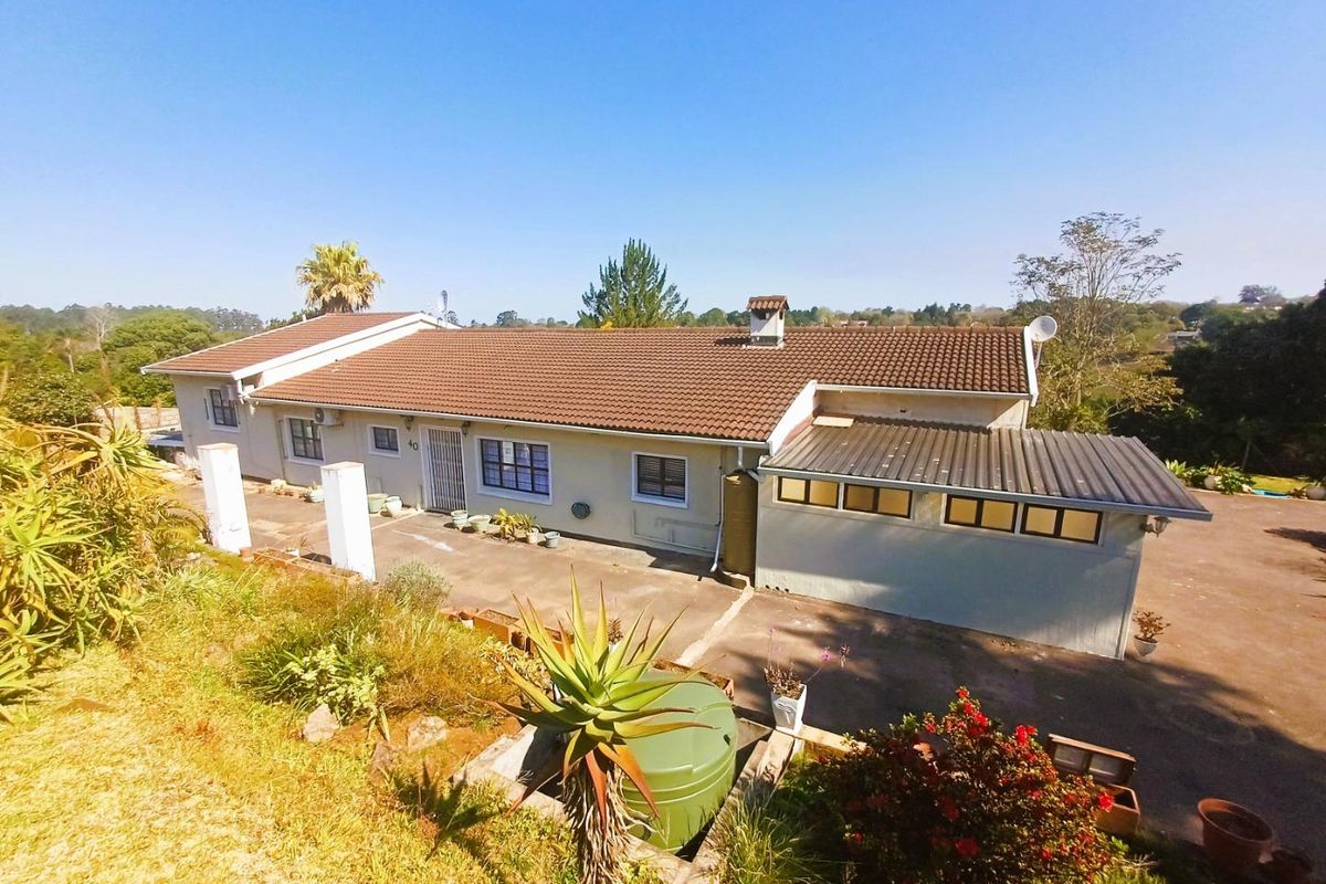 Rear view of a single-story house featuring a tiled roof, concrete patio area, and a water tank, set within a spacious garden.
