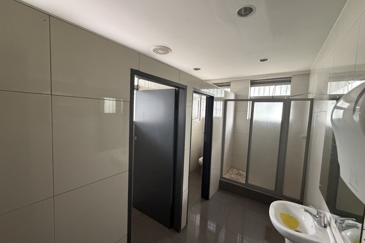 A functional industrial-style bathroom featuring tiled walls and flooring, a pedestal sink, and a separate shower enclosure with glass doors.