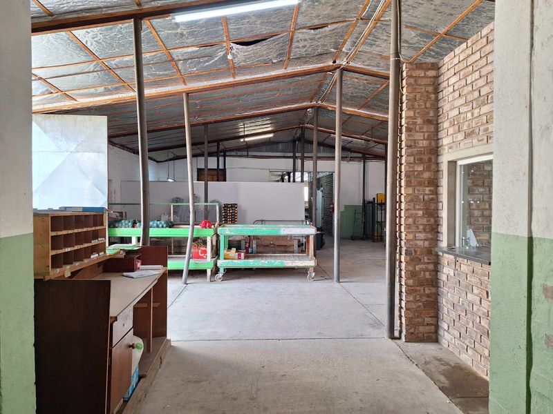 Industrial utility space featuring exposed roof structure, concrete flooring, and a brick service window, suitable for storage or workshop operations.
