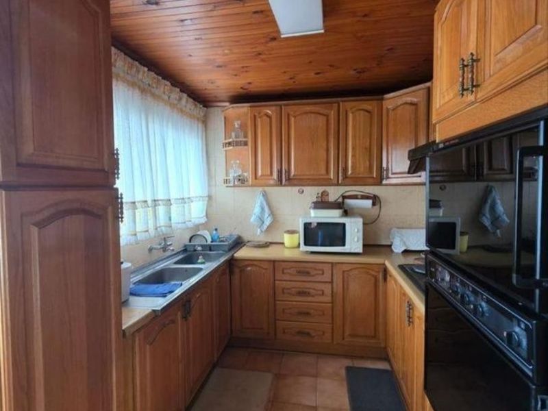 A dated kitchen featuring extensive wooden cabinetry, a timber-paneled ceiling, built-in oven, and tiled flooring, offering significant potential for a modern renovation.