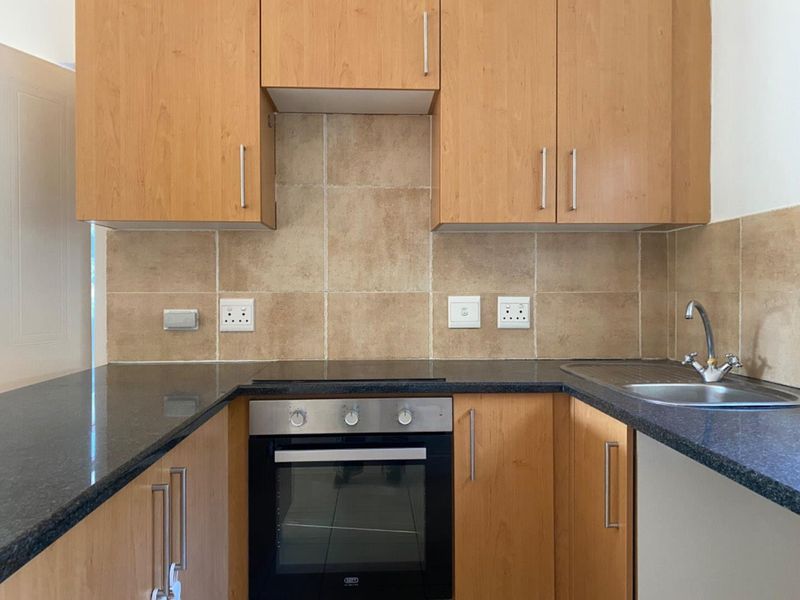 A functional kitchen featuring wooden cabinetry, granite countertops, a built-in oven with electric hob, and a tiled backsplash.