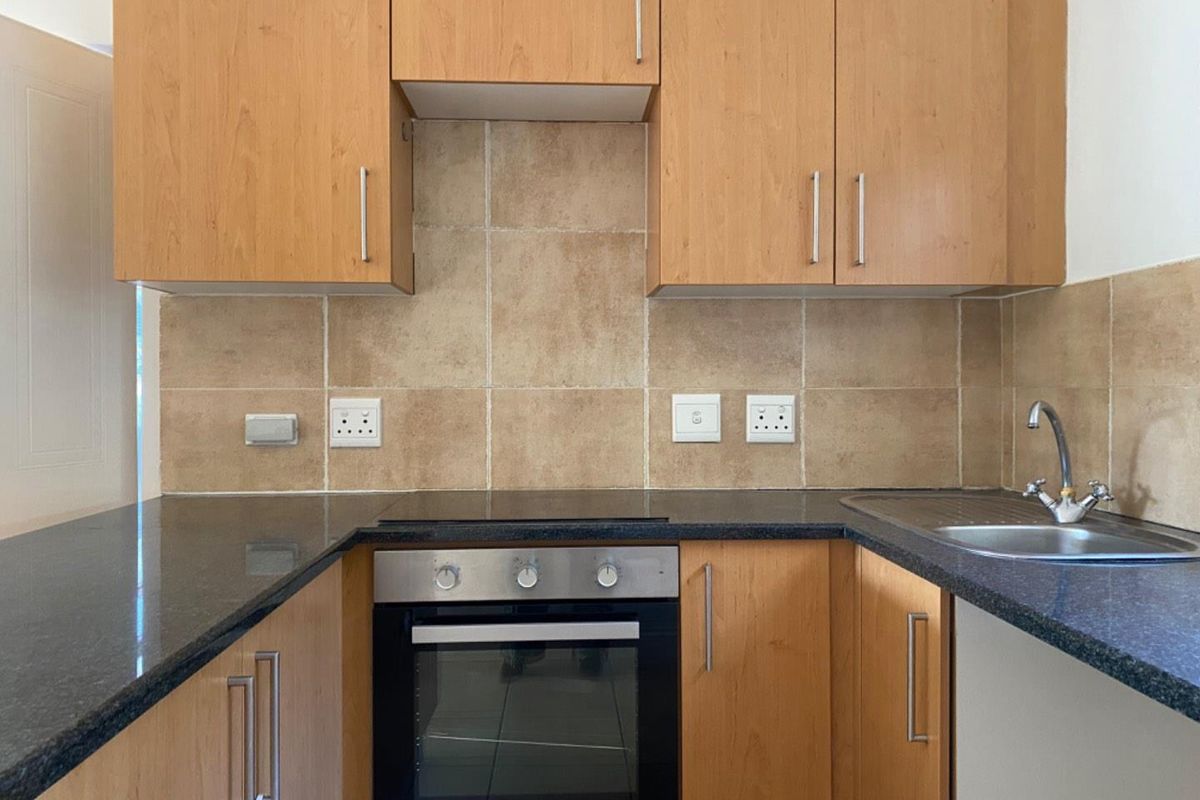 A functional kitchen featuring wooden cabinetry, granite countertops, a built-in oven with electric hob, and a tiled backsplash.