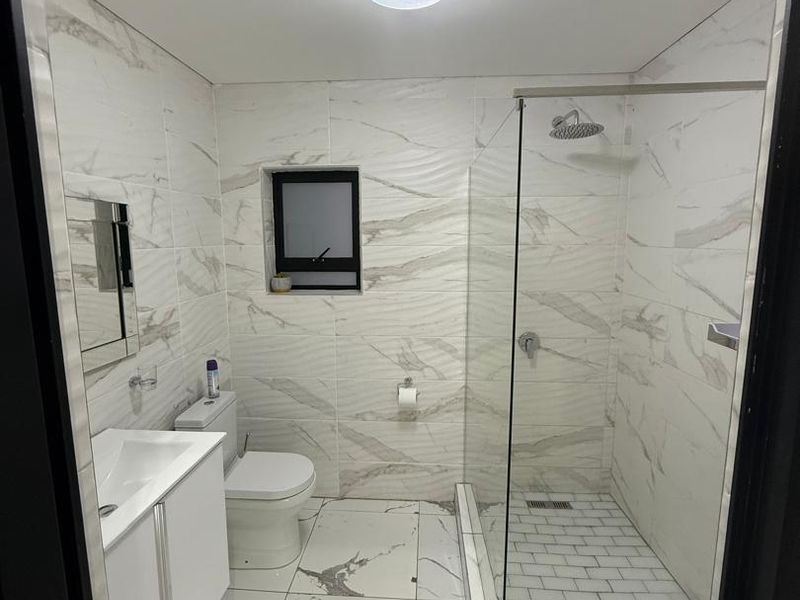 Modern bathroom featuring a walk-in shower with glass screen, vanity cabinet with basin, and contemporary marble-look wall and floor tiling.