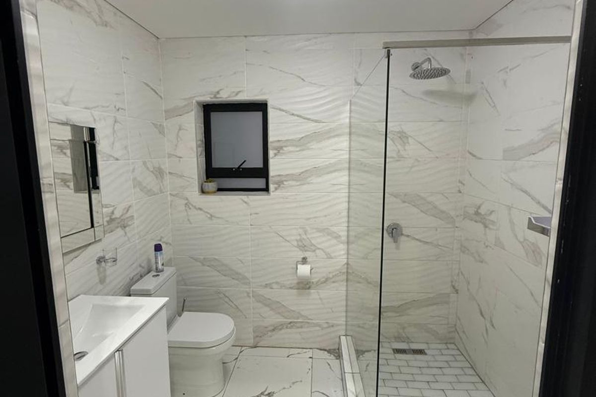 Modern bathroom featuring a walk-in shower with glass screen, vanity cabinet with basin, and contemporary marble-look wall and floor tiling.