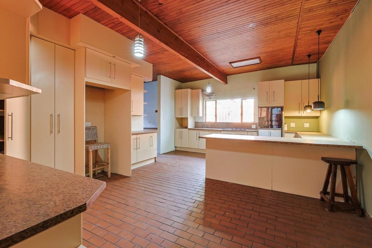 Spacious kitchen featuring a timber-paneled vaulted ceiling, ample cabinetry, a breakfast bar, and durable brick flooring.