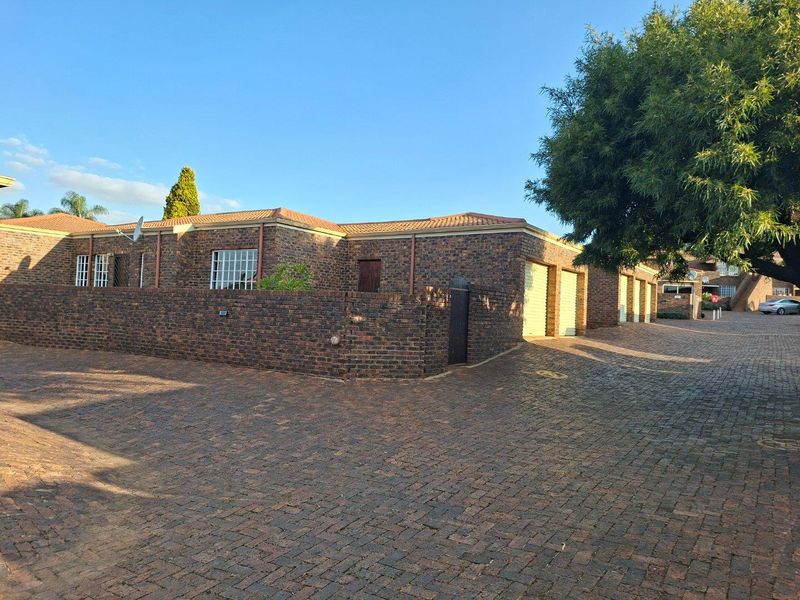Exterior view of a facebrick townhouse featuring a paved driveway, multiple garage doors, and secure boundary walling.