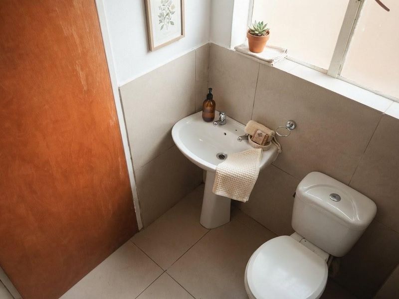 A compact bathroom featuring a pedestal basin, toilet, and neutral wall and floor tiling.