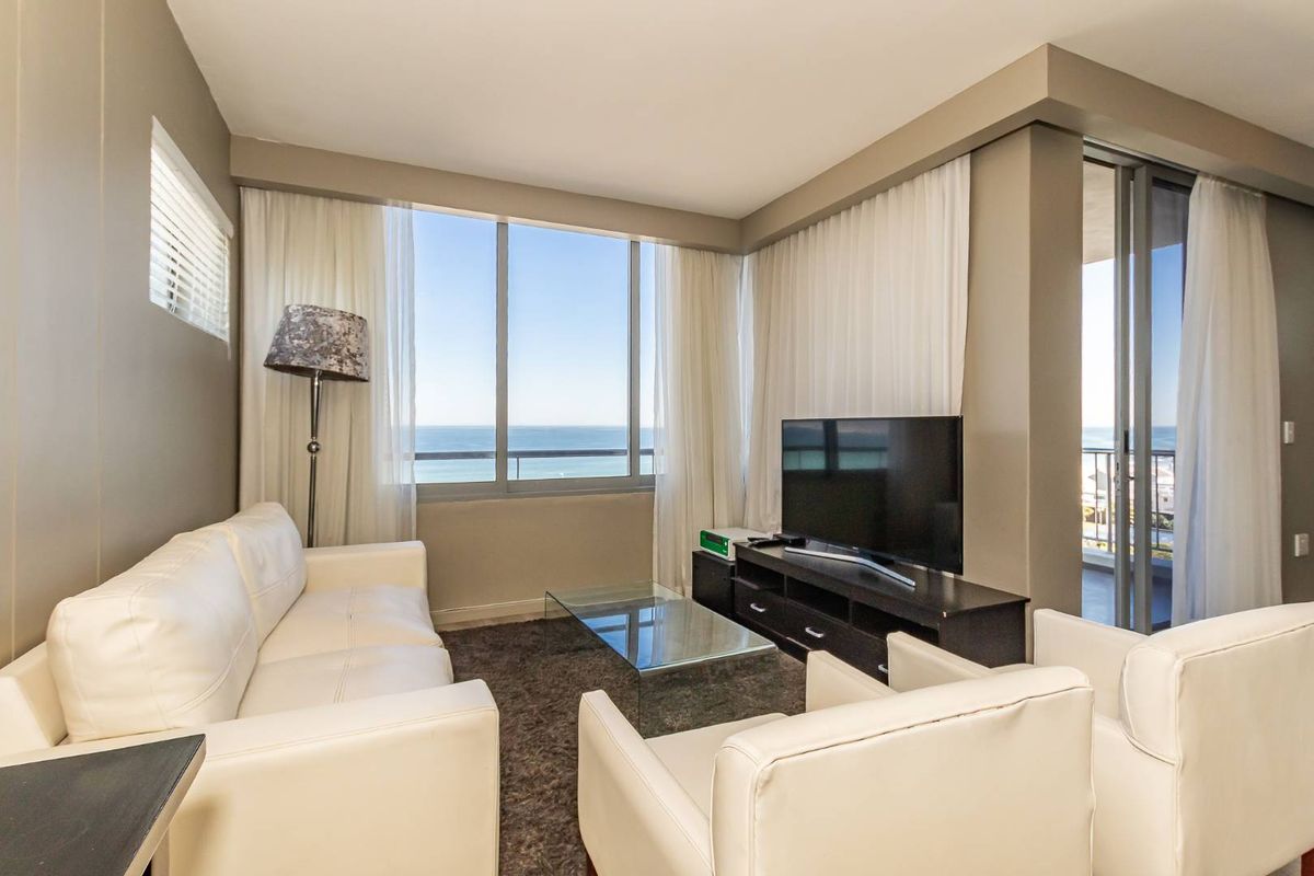 A bright living room featuring large windows with ocean views and direct access to a private balcony, creating a seamless indoor-outdoor living experience.