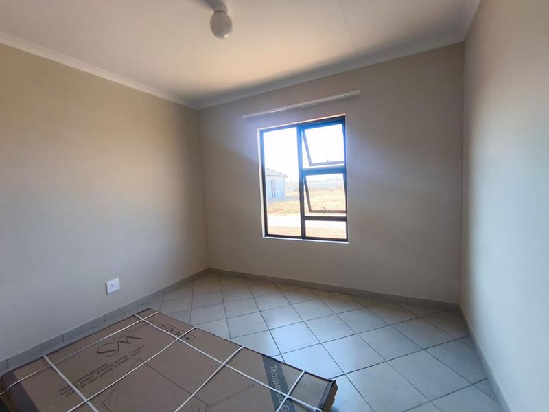 A clean, empty bedroom featuring neutral wall paint, tiled flooring, and a modern aluminium window frame, offering a blank canvas for interior design.