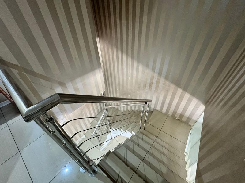 A staircase featuring a modern stainless steel balustrade and tiled steps, currently showing signs of wear on the wallpapered walls.