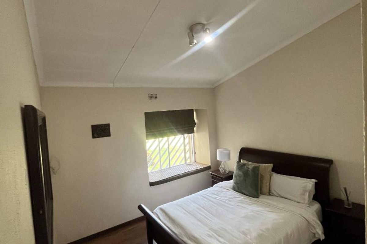 A bedroom featuring wood-look flooring, a recessed window with security bars, and a central ceiling light fixture.