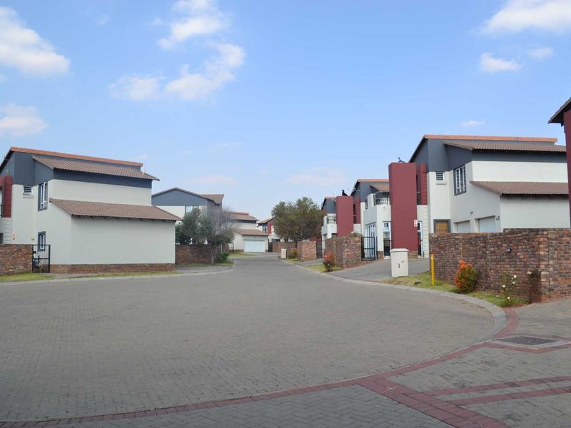 A view of a residential street within a housing complex, featuring modern homes with paved driveways and brick boundary walls.