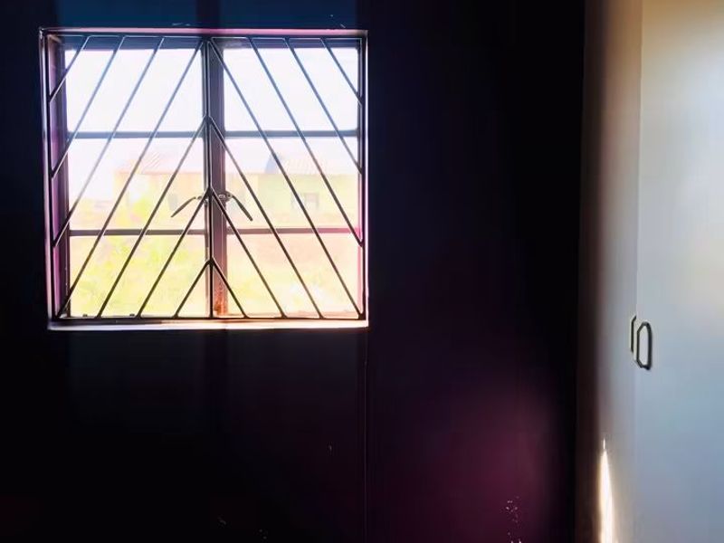An empty bedroom featuring tiled flooring, a built-in cupboard, and a window fitted with security bars.