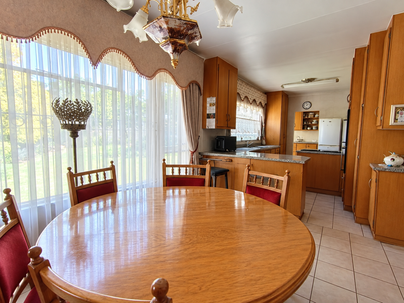 Open-plan kitchen and dining area featuring traditional wooden cabinetry, tiled flooring, and ample natural light from large windows.