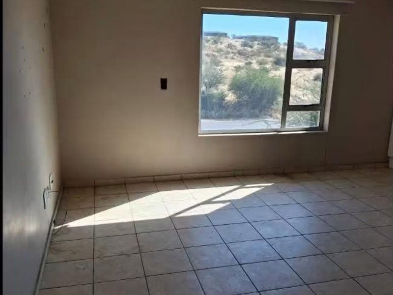 An empty living room featuring tiled flooring and a large window with natural light, offering a blank canvas for potential renovation and interior design.