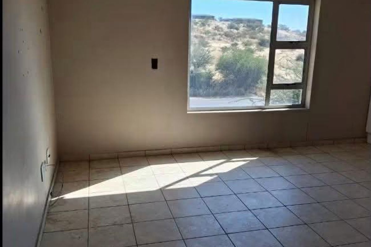 An empty living room featuring tiled flooring and a large window with natural light, offering a blank canvas for potential renovation and interior design.