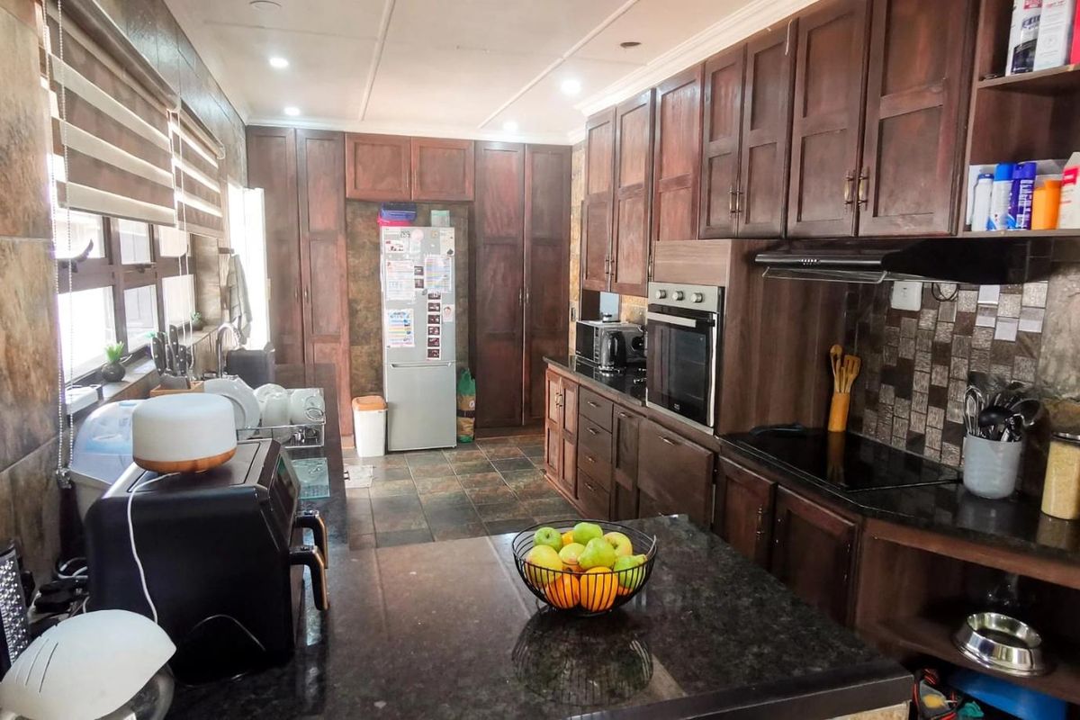 A functional kitchen featuring dark wood cabinetry, granite countertops, built-in oven, electric hob, and tiled wall finishes.