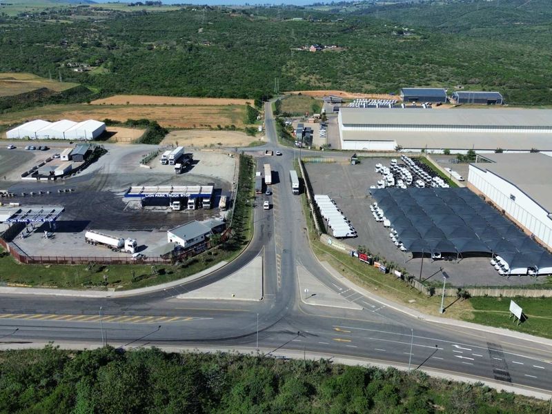 Aerial view of an industrial truck stop facility featuring large warehouses, fueling stations, shaded parking areas, and direct access to the main road network.