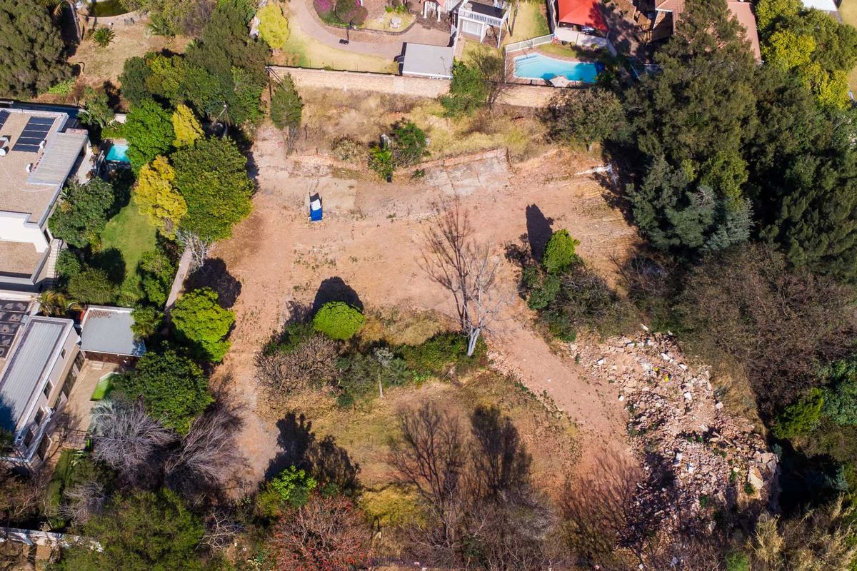 An aerial view of a vacant residential plot featuring mature trees, established boundary vegetation, and some cleared areas ready for development.