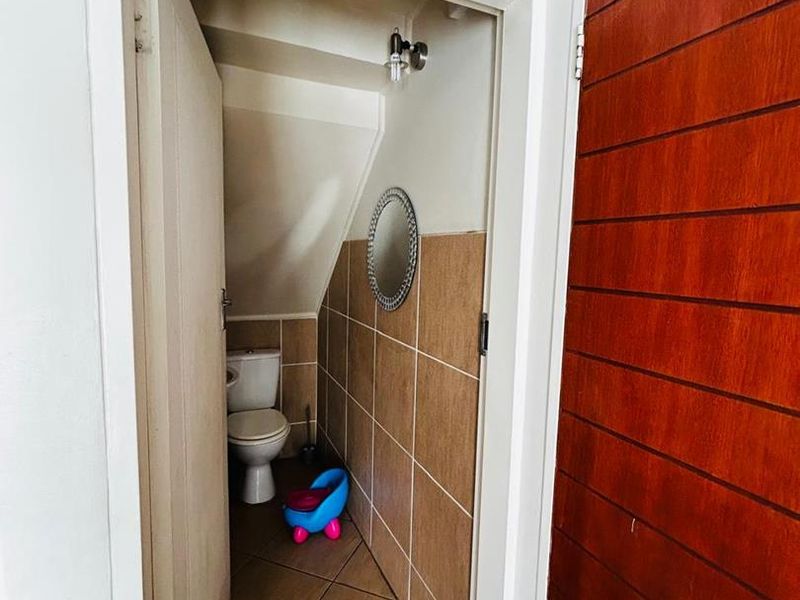 A compact guest bathroom featuring tiled walls and flooring, situated under a staircase with a standard toilet fixture.
