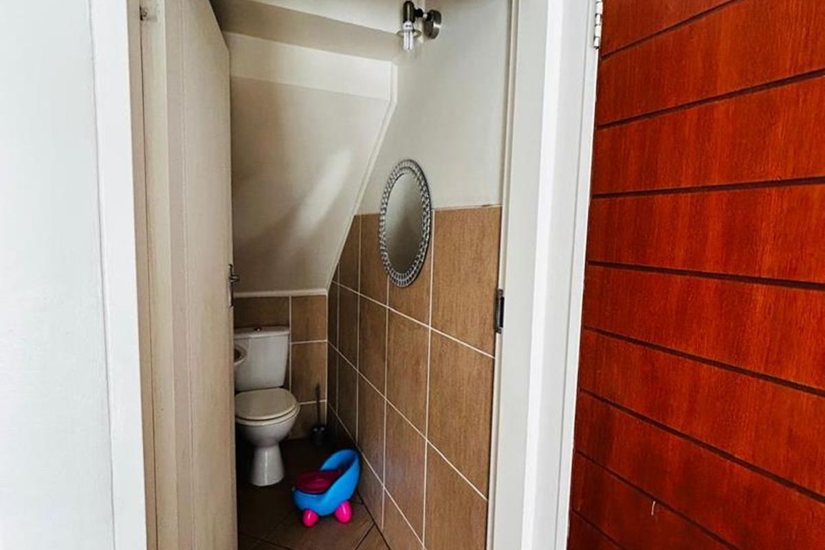 A compact guest bathroom featuring tiled walls and flooring, situated under a staircase with a standard toilet fixture.