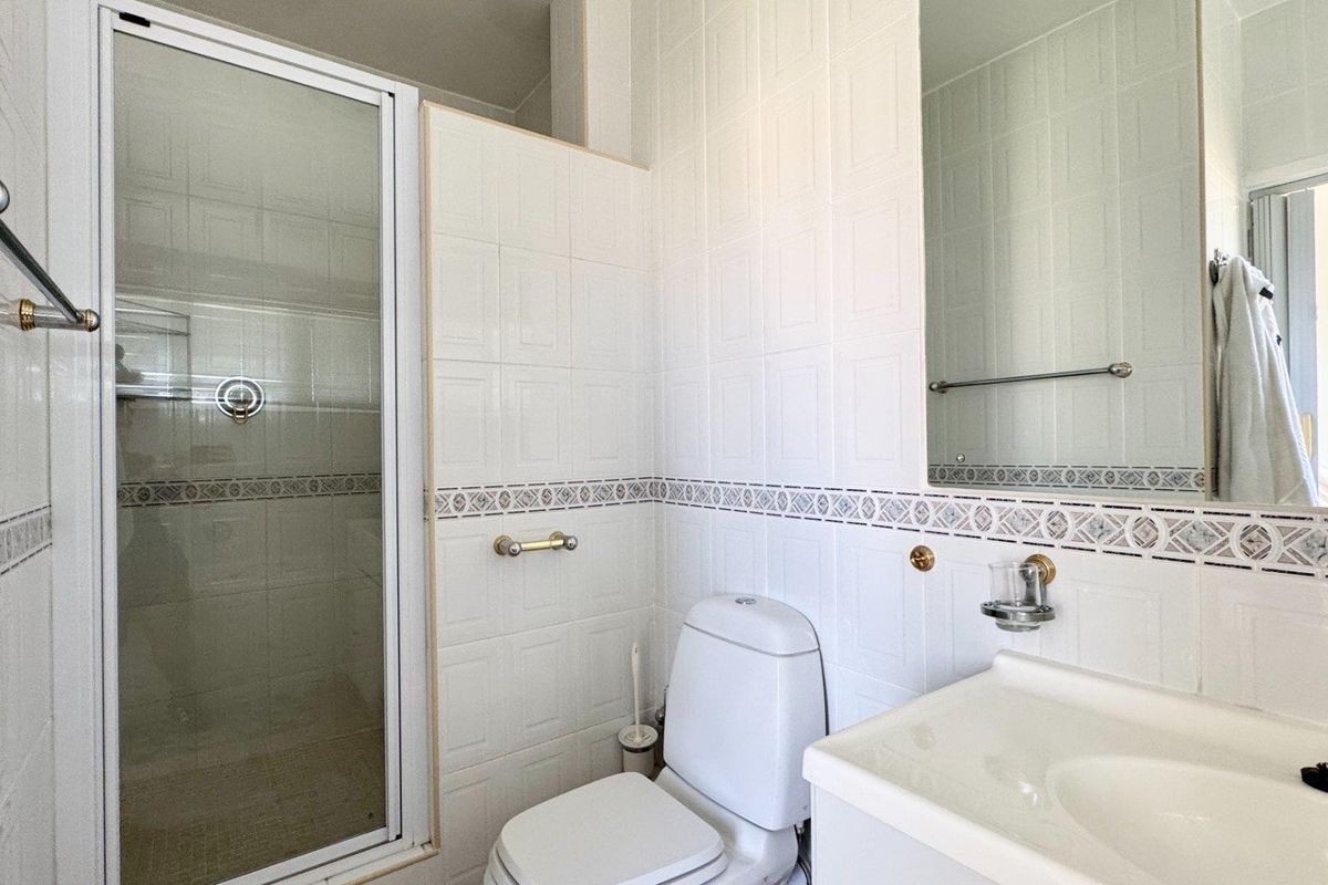 A functional bathroom featuring a shower enclosure, white toilet, and vanity basin with wall-mounted mirror and tiled finishes.