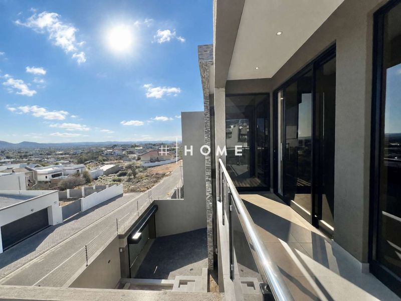 Modern balcony featuring a glass balustrade, recessed lighting, and large sliding doors, offering elevated views of the surrounding neighborhood.