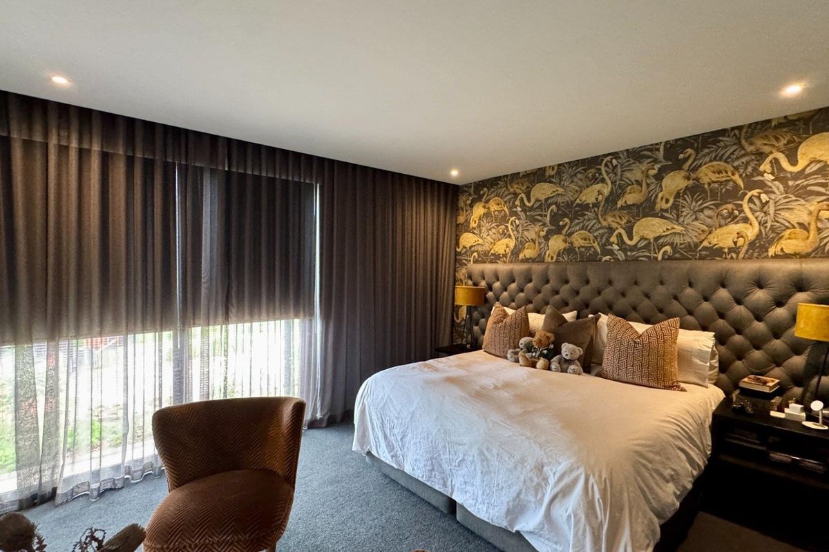 A well-appointed bedroom featuring a tufted headboard, patterned feature wallpaper, and floor-to-ceiling curtains providing ample natural light control.