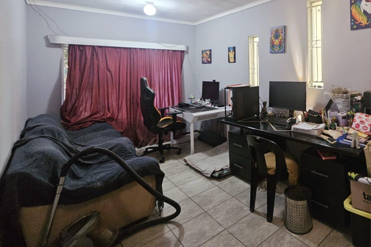 A functional bedroom or home office space featuring tiled flooring, vertical windows, and a neutral wall finish.