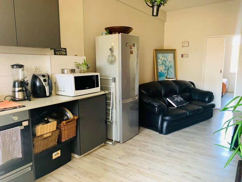 Open-plan living area featuring a compact kitchen with built-in oven, tiled backsplash, and light-toned laminate flooring throughout the combined space.