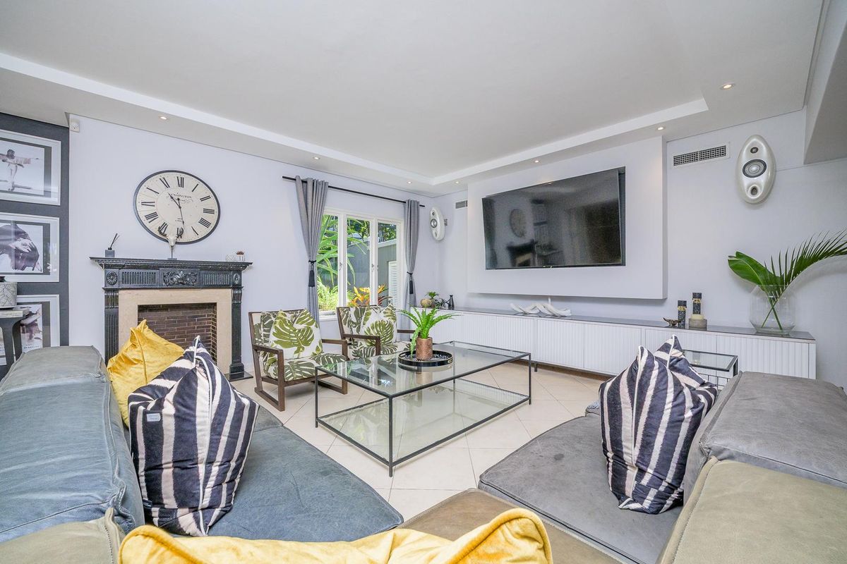 Spacious living room featuring a classic fireplace, built-in media cabinetry, recessed ceiling lighting, and large windows overlooking the garden.
