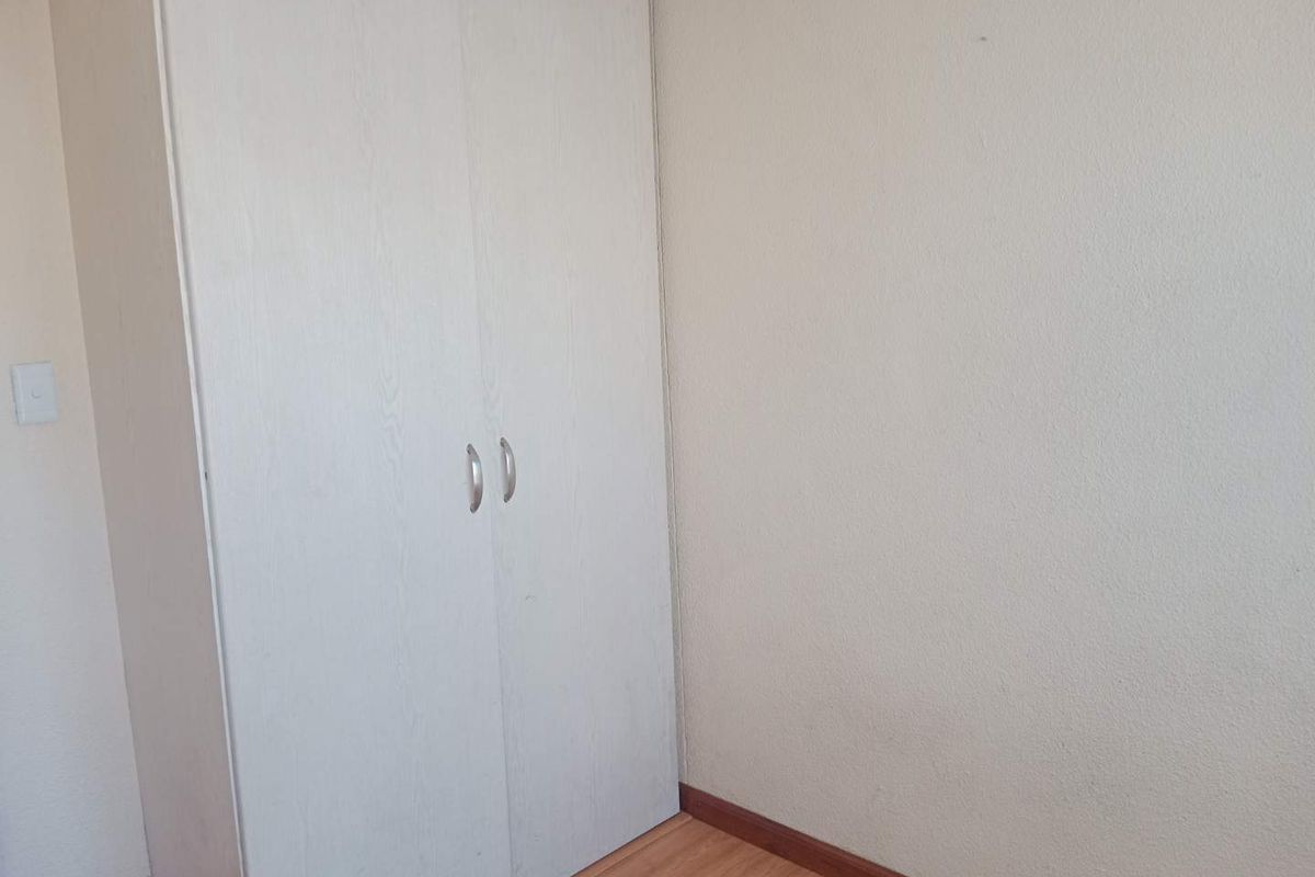 A simple bedroom featuring light-toned laminate flooring and a built-in wardrobe with a neutral finish.