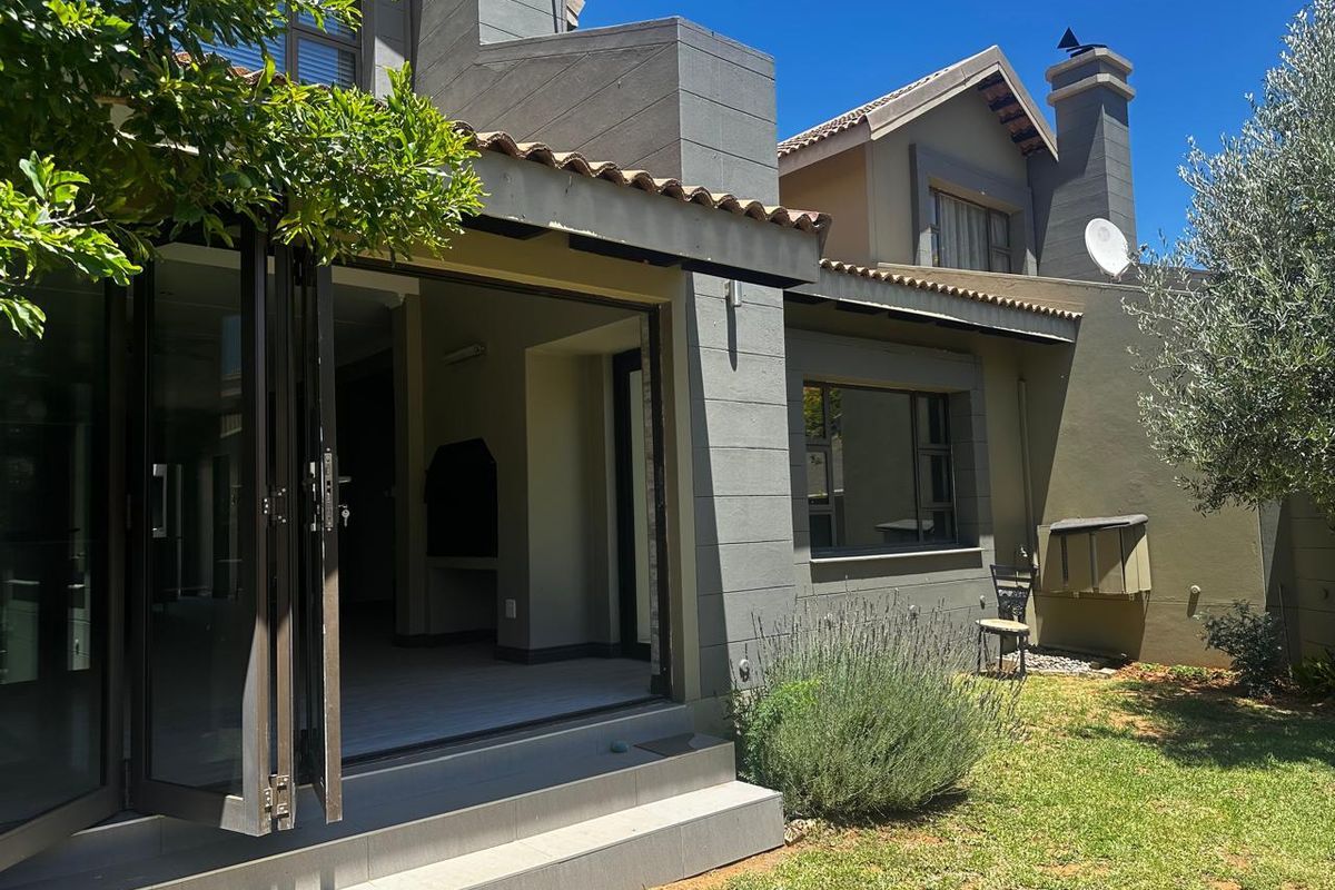 Rear view of the townhouse featuring a covered patio with folding glass doors, tiled steps, and a private garden area.