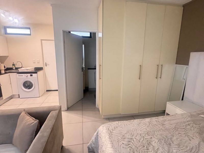 Open-plan living area featuring tiled floors, built-in bedroom cupboards, and an integrated kitchen space with cabinetry and sink.