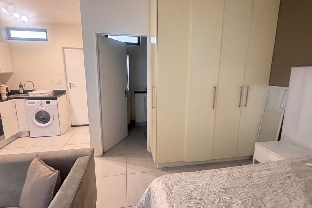 Open-plan living area featuring tiled floors, built-in bedroom cupboards, and an integrated kitchen space with cabinetry and sink.
