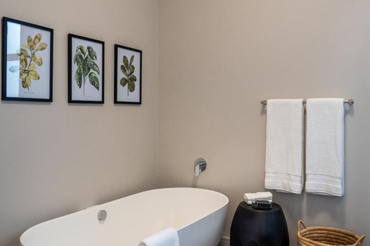 A modern bathroom featuring a sleek freestanding bathtub, wall-mounted faucet, and neutral tiled flooring in a well-maintained space.
