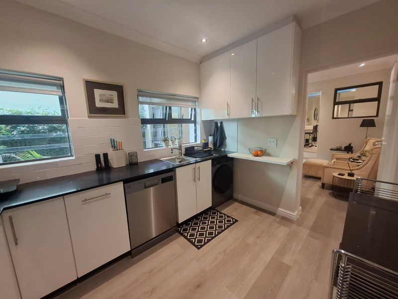 Modern kitchen featuring sleek white cabinetry, dark laminate countertops, integrated dishwasher, and light wood-look flooring, offering a clean and functional workspace.