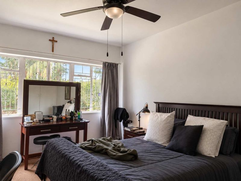A well-lit bedroom featuring a ceiling fan, large windows with security bars, and built-in storage cupboards.