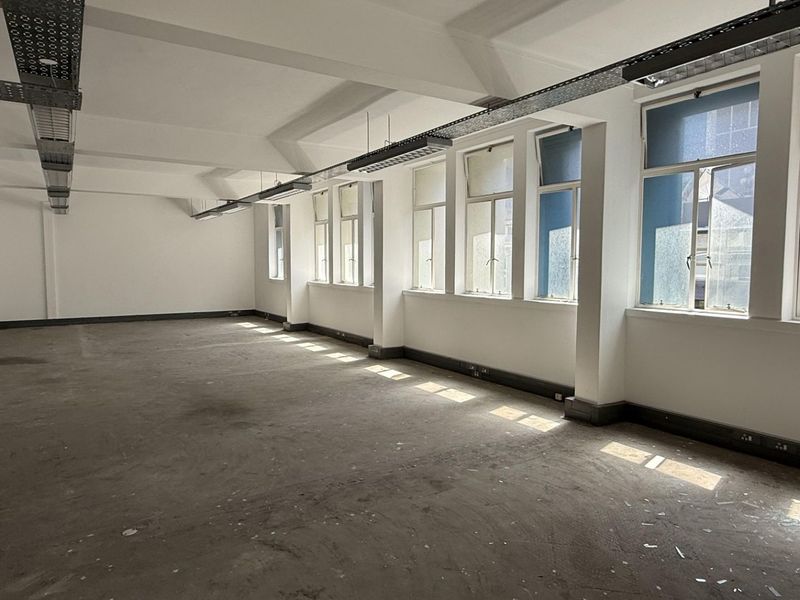 A spacious, empty office area featuring large windows, exposed ceiling cable trays, and neutral walls, ready for custom fit-out.