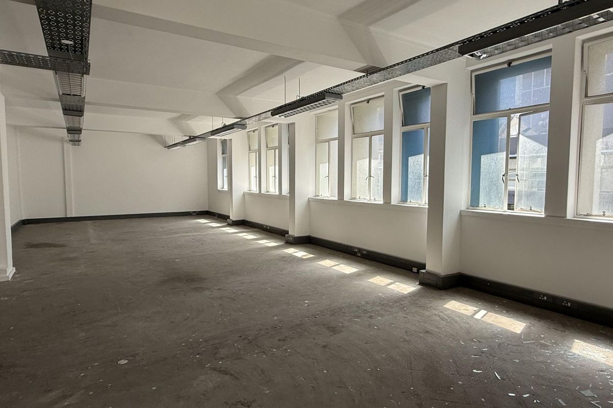 A spacious, empty office area featuring large windows, exposed ceiling cable trays, and neutral walls, ready for custom fit-out.