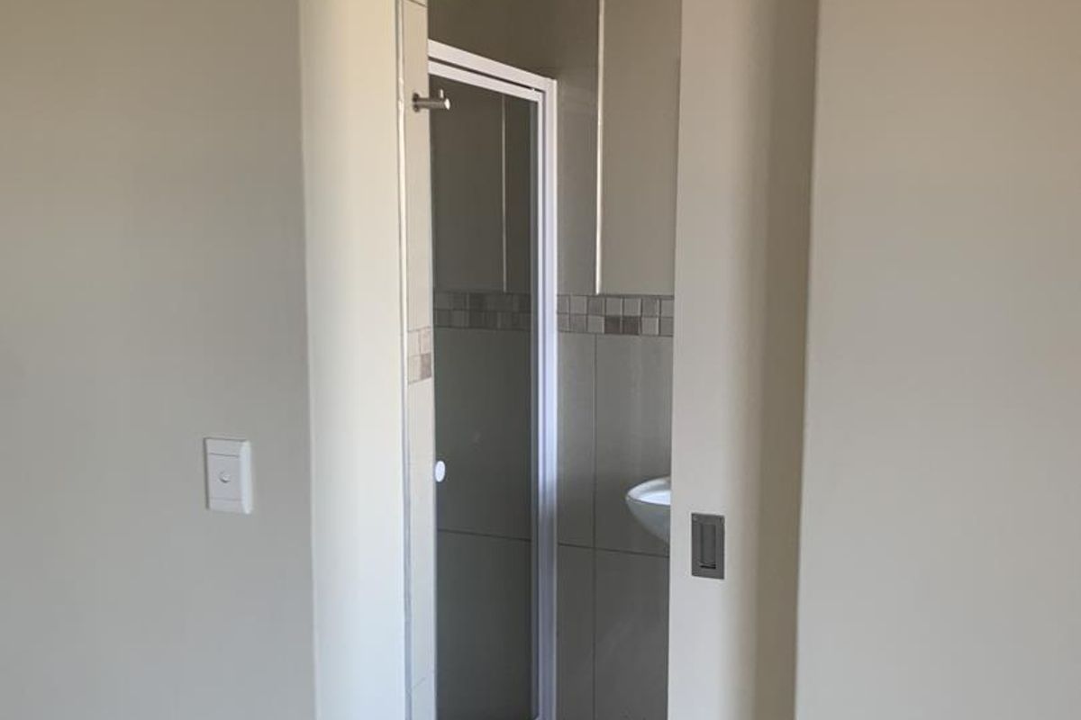 A view through a sliding door into a bathroom featuring a shower enclosure with tiled accents and a wall-mounted basin.
