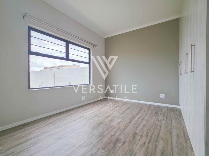 A bright, empty bedroom featuring modern laminate flooring, built-in cupboards, and large aluminium-framed windows.