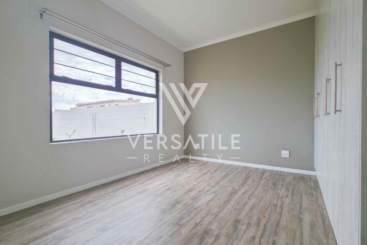 A bright, empty bedroom featuring modern laminate flooring, built-in cupboards, and large aluminium-framed windows.