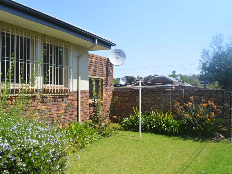 A rear garden area featuring a face brick townhouse exterior, security bars on windows, a satellite dish, and a private lawn with boundary wall.