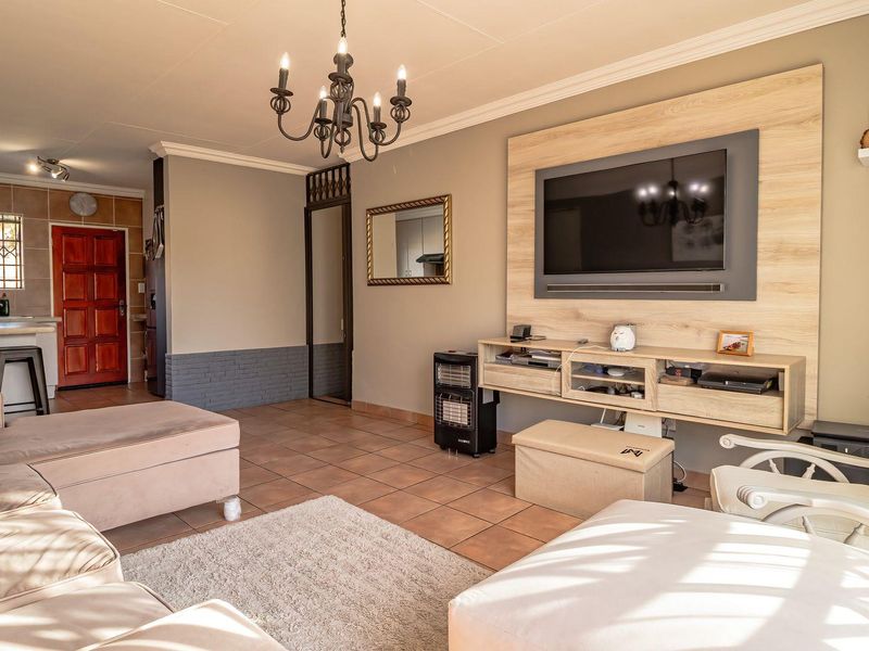 Spacious open-plan living area featuring tiled floors, a modern built-in television wall unit, and a seamless flow into the adjacent kitchen space.